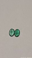 Two oval cut natural emeralds side by side showing matched color and size.