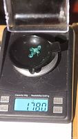Five small round emeralds placed on a small black scale showing total weight 1.78 carats.