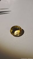 Oval golden-yellow gemstone on white background beside metal tweezers