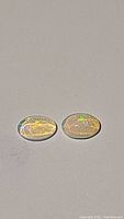 Matched pair of translucent oval Ethiopian opals lying side by side on a gray surface, showing faint rainbow flashes.