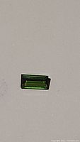 Bright green baguette cut natural tourmaline gemstone photographed on a light background showing sharp rectangular shape and bright color.