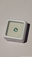 Round faceted light green gemstone in white display box