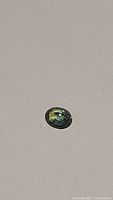 Close-up image of the oval cut sapphire showing blue, green, and yellow colors.