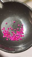 Close-up of loose tiny ruby stones in black container showing vivid color and faceting