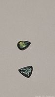 Two small tri-colored sapphires, one pear shaped and one triangular, visible on plain background.