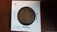 Front side of the 1859 Canadian Large One Cent coin showing the shield and emblems, secured in a white cardboard holder.