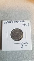 Front view of 1947 Newfoundland 10 cent coin placed in protective cardboard holder with denomination and date clearly visible.