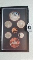 Coins displayed in black leather-like Nortel branded case, six circulating coins plus silver dollar commemorative coin visible under clear cover.