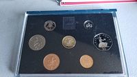 Clear view of all seven coins arranged in display case with clear plastic cover and black background.