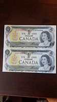 Two 1973 Canadian $1 bills front side showing sequential serial numbers 8CN990868 and 8CN990869 and Queen Elizabeth II portrait.