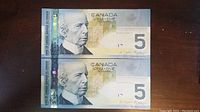 Front view of two Canadian $5 polymer banknotes placed one above the other showing Sir Wilfrid Laurier portrait and holographic security features.