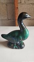 Photo of a glazed ceramic goose figurine with dark green and black colors, glossy finish, and smooth surface.