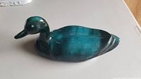 Photo of a ceramic duck figurine with teal green and dark green colors, placed on a white surface.