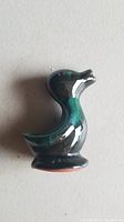 Top view of a glossy ceramic baby duck figurine glazed in dark green hues with a visible small chip on the tail area.