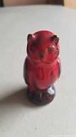 Close-up of small red glazed owl figurine standing upright on a flat surface.