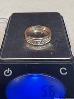 Ring on digital scale showing a 5.6g weight reading and front view of textured pattern.