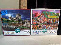 Photo showing two Buffalo brand puzzle boxes, one 750 piece puzzle with a castle scene and one 1000 piece puzzle with a colorful country life scene.