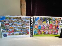 Photo of two 1000-piece puzzles side by side, showing their front box covers. One puzzle is Globetrotter United Kingdom with UK landmarks and scenes, the other is Home Tweet Home showing colorful birdhouses.