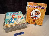 Photo of the stack of 15 vintage children's Little Golden Books with Woody Woodpecker Takes a Trip on top and Walt Disney's Pinocchio displayed upright.