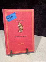Red hardcover book front cover with title 'The House at Pooh Corner', author A. A. Milne, and image of Winnie the Pooh embossed in gold and black.