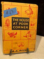 Front cover of the book showing title 'The House at Pooh Corner' with Winnie the Pooh character illustrations and author name A.A. Milne.