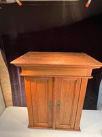 Front view of the antique late Victorian wooden hanging cupboard. Shows the cupboard standing alone with two paneled doors and brass keyhole escutcheons.