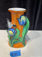 Front side of the antique Art Deco orange ceramic vase showing blue and yellow tulip flowers with green leaves and a small bird in relief decoration.