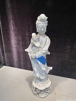 Front view of white porcelain Asian statue figurine holding flower on detailed base.
