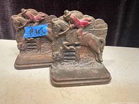 Pair of cast iron book ends featuring a jockey on a horse mid-jump over a fence with some red paint on the rider's jacket.