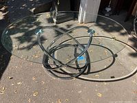 Top and angled view of oval beveled glass coffee table with chrome base outdoors with some leaf debris on the glass surface, showing overall construction and condition.