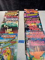 Photo showing 12 vintage comic books arranged in two stacks, with titles visible including Fantastic Four, Defenders, Portal Press, Firestorm, Millennium Legionnaires, Star Trek, Marvel Universe, and Martian Manhunter.