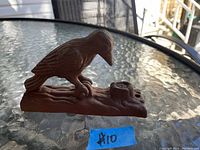 Side view of the cast iron woodpecker door knocker resting on a glass table, showing the bird perched on a tree stump base with a measuring tape placeholder.