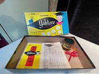 Photo of vintage Yahtzee game components including box, dice, score sheets, instruction manual, and dice shaker.
