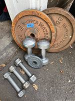 Photo showing two large rusty 35 lbs Whipper Watson weight plates, smaller 1.5 lbs weight plate, two pairs of dumbbells (3.3 lbs and 3 lbs), and one 5 lbs dumbbell.