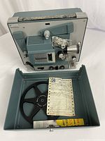 Projector mounted in lower case half with film reel, instruction sheet, and lamp box.