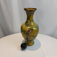 Front view of a large yellow cloisonné vase with floral motifs and a green glass apple for size reference