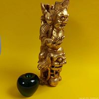 Full view of the antique Asian gilt wood guardian deity mounted on a Fu Dog with a green apple for size reference.