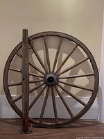 Antique wooden wagon wheel leaning against wall with wooden yoke beam in front