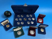 Green apple size reference beside velvet-lined blue case and individual coin cases on blue background