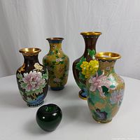 Four antique Asian cloisonné vases placed together with a green apple for size reference, showing floral motifs and gold rims.