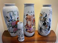 Three large and one small Asian vases arranged on wooden table, showing detailed decorative paintings and shapes