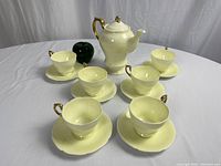 Full set of coffee pot, six cups and saucers arranged on table with green apple for scale