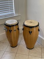 Pair of conga drums side by side on tiled floor under window light