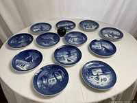Twelve blue and white Royal Copenhagen collector plates arranged on a round table with a green apple for scale.