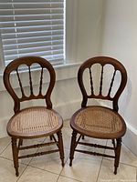Two matching antique pine chairs with cane webbed seats and curved backs with spindle supports, placed side by side.