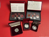 Photo of two black folders with Canadian coin year sets containing multiple coins each, plus three silver dollar coins in protective cases.