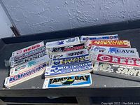 Wide view of multiple sports team bumper stickers laid out on table showing variety of teams.