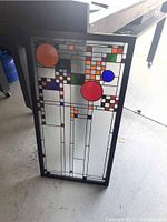 Front view of stained glass window panel showing the full geometric design with colored glass circles and squares in a black frame.