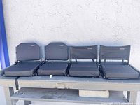 Four black Sheenwle brand portable stadium chairs in a row showing foldable design and padded cushions.