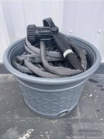 Top view of grey polymer hose storage pot containing coiled grey expandable garden hose and black Orbit Pro nozzle